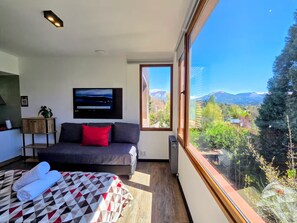 A bedroom with a bed, a sofa, a TV, and a large window with a mountain view. - #7 Modern Loft with Fast WiFi, Great for Remote Work. 300 m from the Lake (San Carlos de Bariloche)