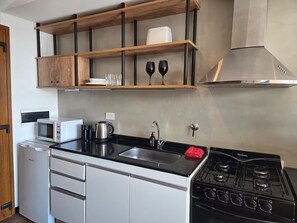 A compact kitchen with a black stove, white cabinets, a microwave, and a wooden shelf above the sink. - #7 Modern Loft with Fast WiFi, Great for Remote Work. 300 m from the Lake (San Carlos de Bariloche)