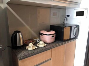 Eine kleine Küche mit einer Mikrowelle, einer Kaffeemaschine und einem Reiskocher auf der Arbeitsplatte.