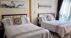 Zwei Betten mit weißen Laken und Zierkissen, ein Bild an der Wand und ein Fenster mit Vorhängen.