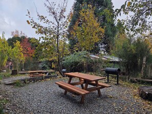 An outdoor picnic area with a wooden table and benches, surrounded by trees and gravel. - #6 Comodo y luminoso Loft a 300 metros de Playa Bonita y a 12 km de Catedral (San Carlos de Bariloche)