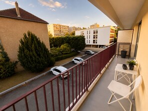A balcony with a red railing, a white table with chairs, and a view of parked cars and buildings. - Elegant studio apartment with a balcony and parking in Metz (Metz)
