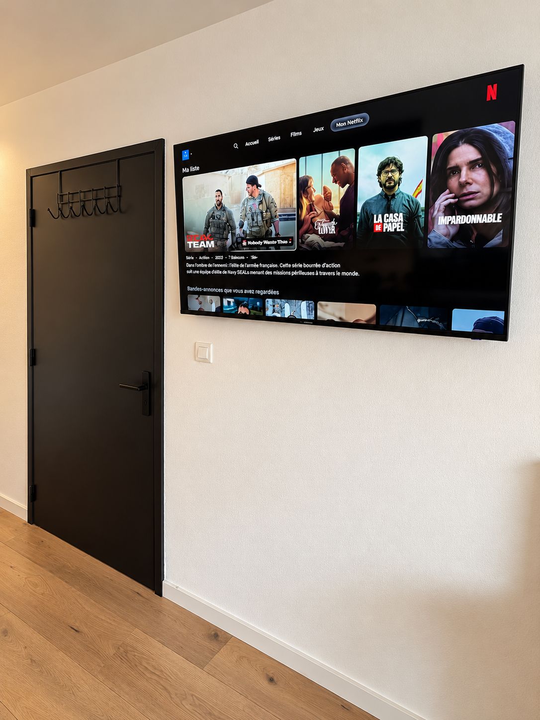 Un televisor montado en la pared muestra una interfaz de Netflix con diversas opciones de películas.