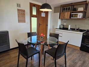 Een kleine keuken met een ronde glazen tafel, zwarte stoelen, een magnetron en een kookplaat.