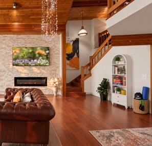 Amplia sala de estar con un sofá de cuero, chimenea, escalera y estantería.