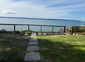 Un sendero conduce a una propiedad frente al agua, con baranda de madera y vista al mar.