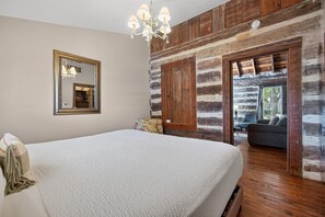 A bedroom with a large bed, a chandelier, a mirror, and a view of an outdoor seating area. - Historic Cabin w/King Bed + Walk to Wineries! (Fredericksburg)
