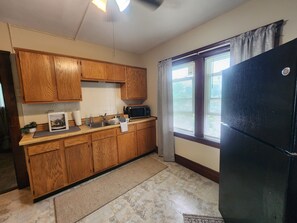 A kitchen with wooden cabinets, a microwave, a refrigerator, and a window with blinds. - Simple & Cozy Cleveland Getaway (Cleveland)