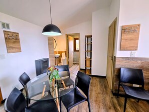 Ein moderner Essbereich mit einem Glastisch, schwarzen Stühlen, einer Pendelleuchte und Holzboden.