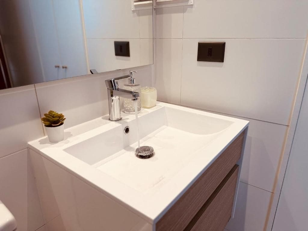 A modern bathroom with a white sink, a mirror, and a small potted plant.