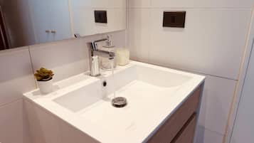 A modern bathroom with a white sink, a mirror, and a small potted plant.