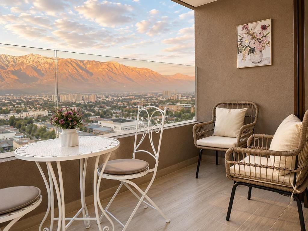 A balcony with a view of mountains, a white table with a vase of flowers, and wicker chairs.