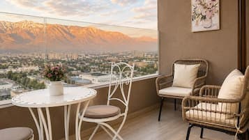 A balcony with a view of mountains, a white table with a vase of flowers, and wicker chairs.