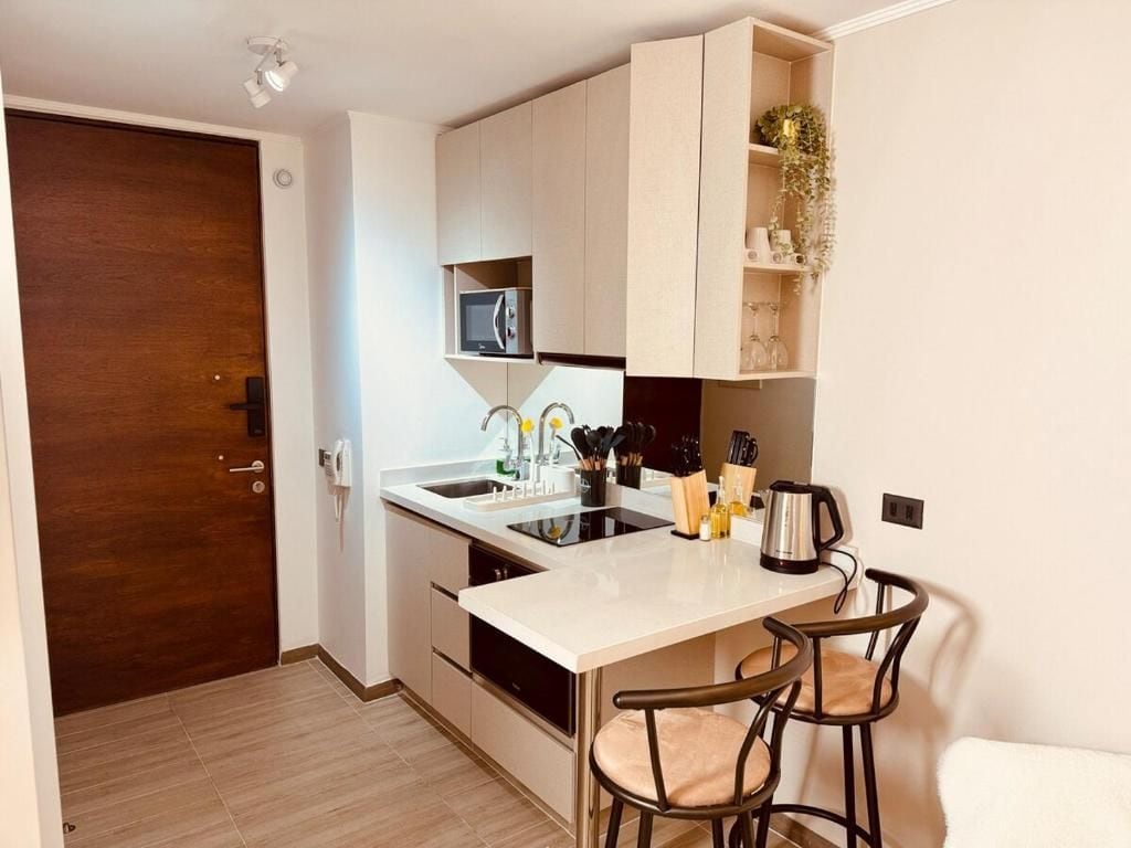 A compact kitchen with a built-in microwave, a coffee maker, and bar stools.
