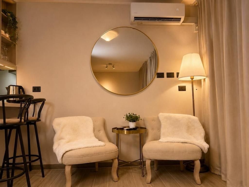 A hotel room with two armchairs, a small round table with a plant, a lamp, and a large mirror on the wall.