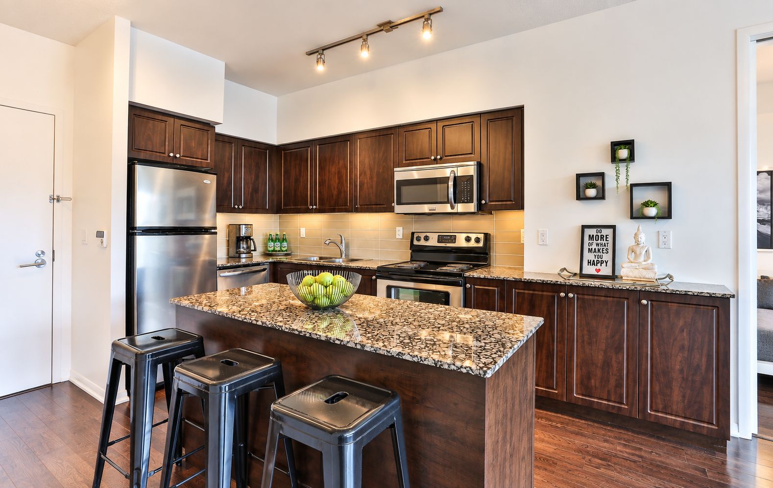 A modern kitchen with dark wood cabinets, stainless steel appliances, a granite countertop, and a central island with stools.