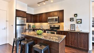 A modern kitchen with dark wood cabinets, stainless steel appliances, a granite countertop, and a central island with stools.