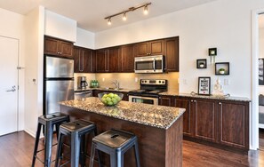 A modern kitchen with dark wood cabinets, stainless steel appliances, a granite countertop, and a central island with stools. - Spectacular Presidential Loft - Downtown Toronto (Toronto)