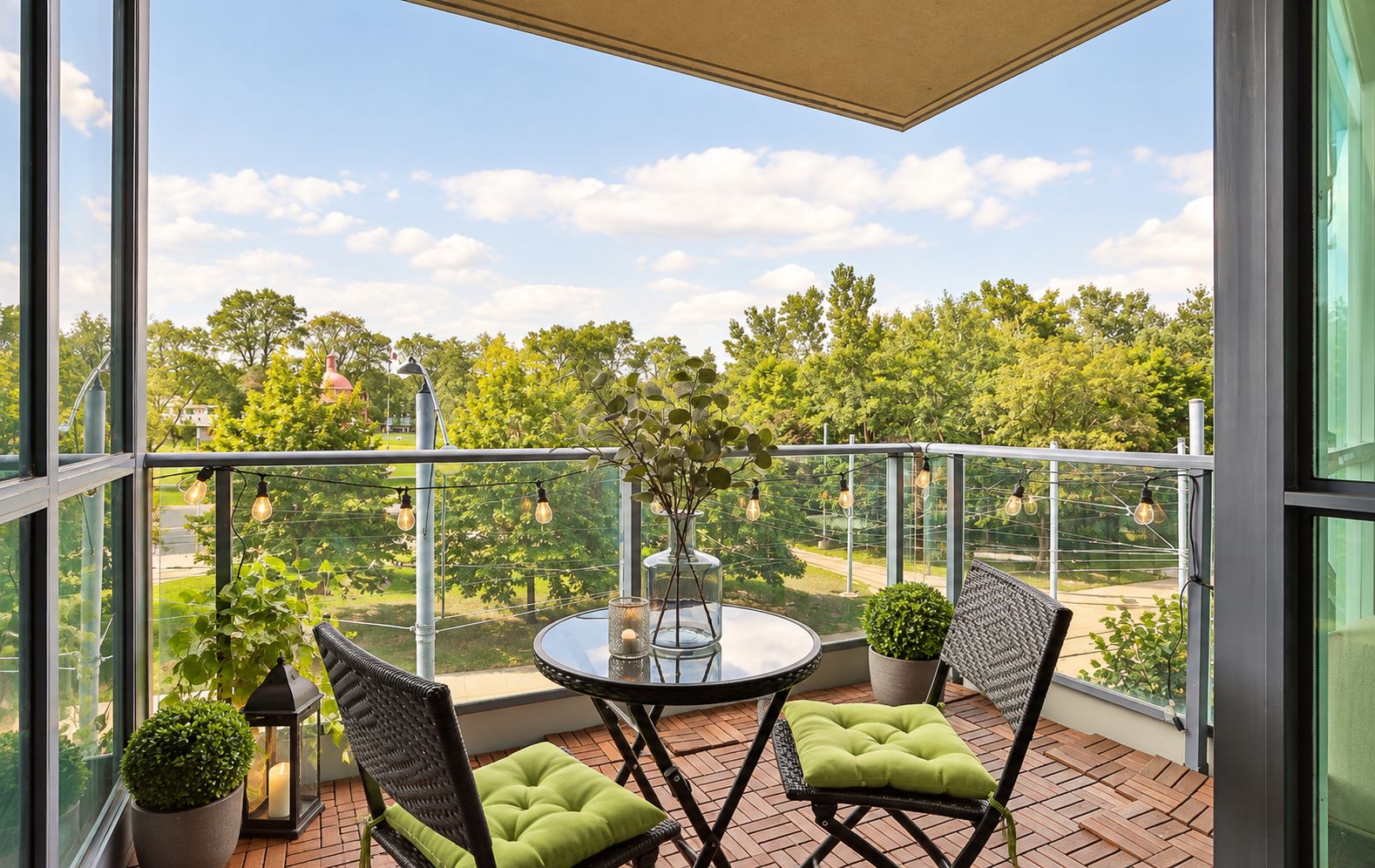A balcony with a round table, two chairs, potted plants, and string lights.