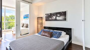 A bedroom with a large bed, a view of the outdoors through a sliding door, and a painting on the wall.