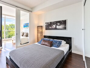 A bedroom with a large bed, a view of the outdoors through a sliding door, and a painting on the wall.