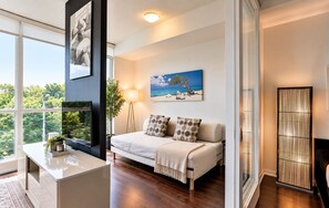 A modern living room with a sofa, a flat-screen TV, a large window, and a painting of a beach scene.