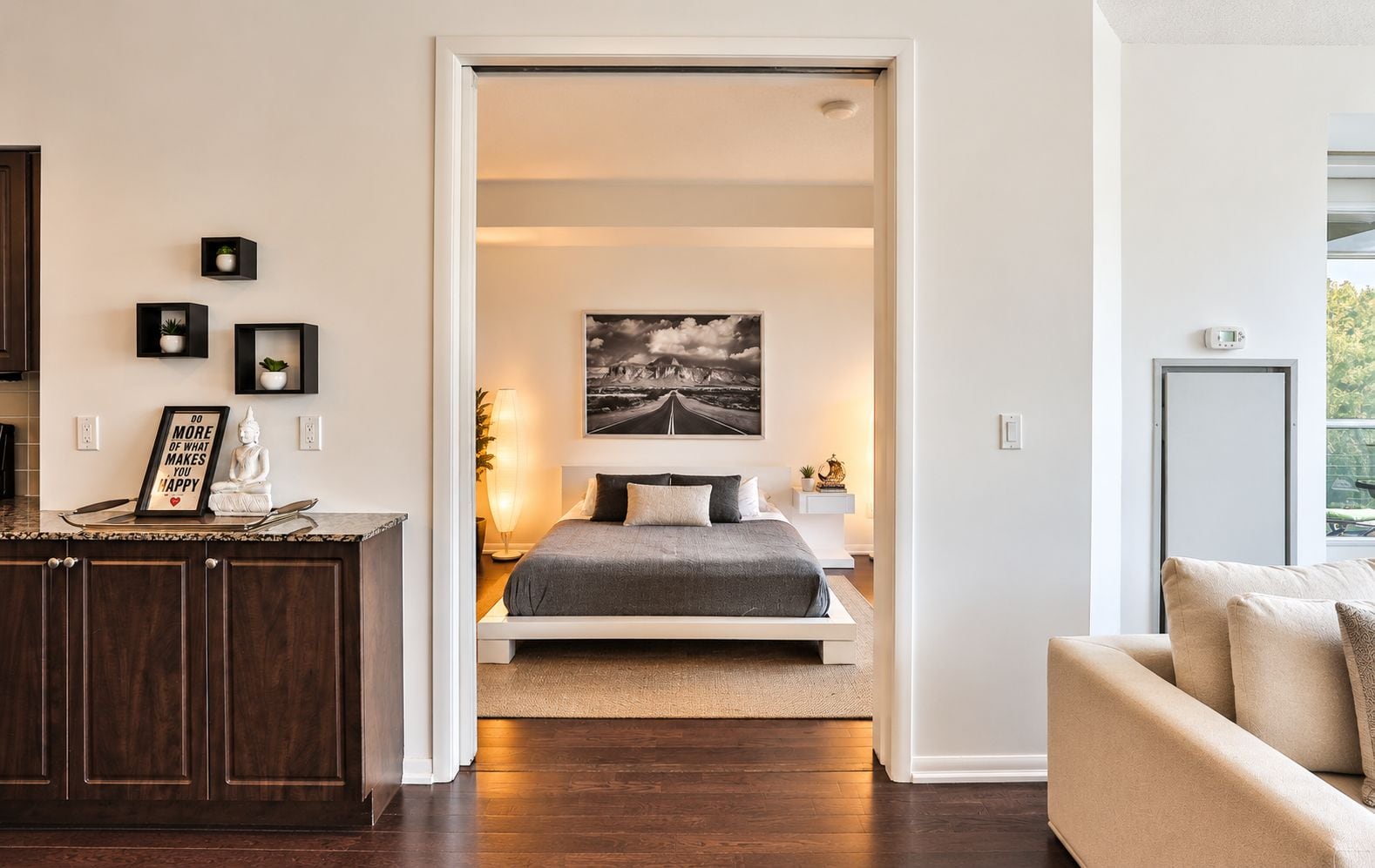 Quarto moderno com cama, mesa de cabeceira e vista para a sala adjacente.