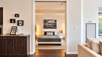 Quarto moderno com cama, mesa de cabeceira e vista para a sala adjacente.