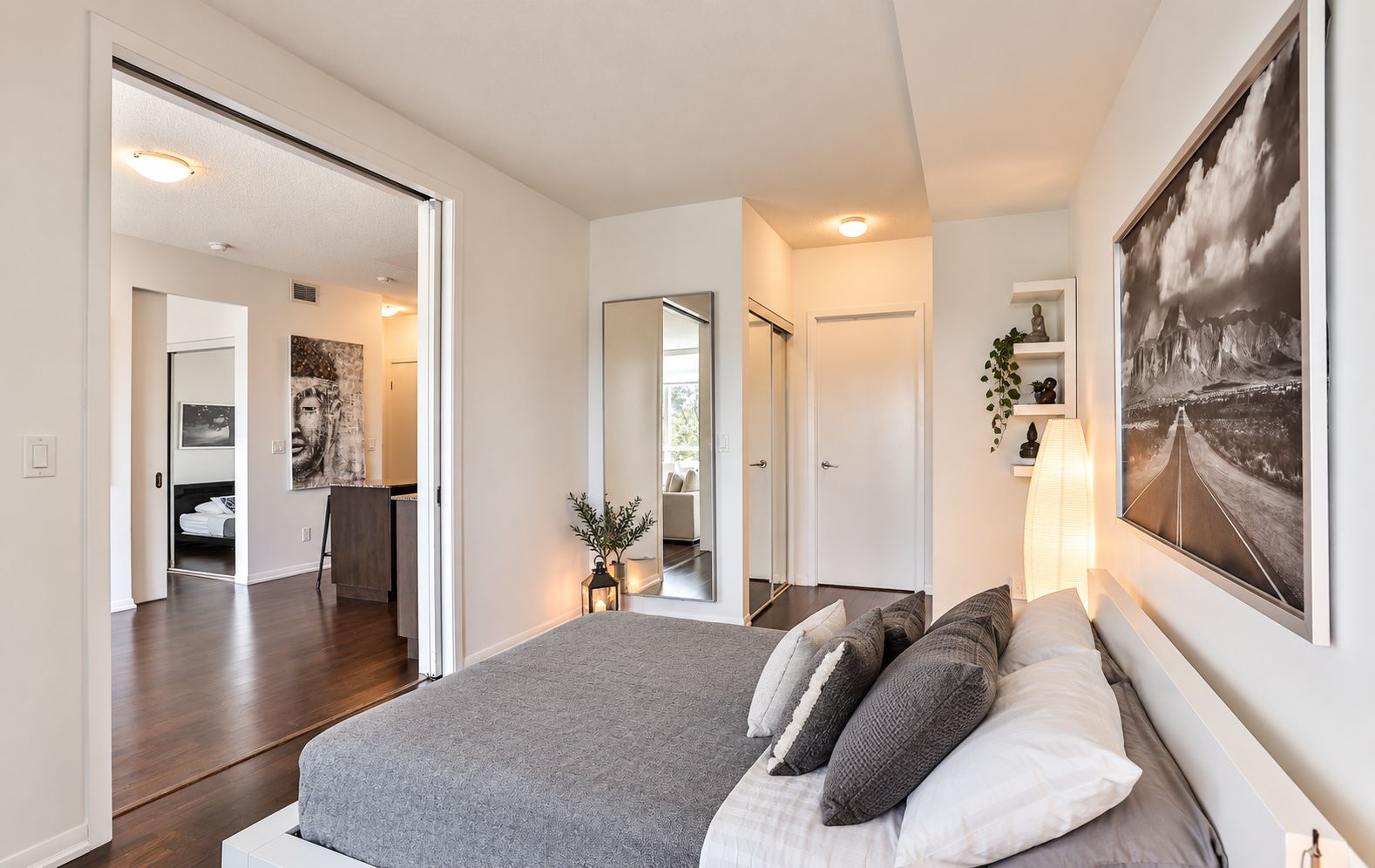 A modern bedroom with a large bed, a mirror, a painting, and a view of the hallway.