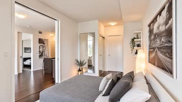 A modern bedroom with a large bed, a mirror, a painting, and a view of the hallway.
