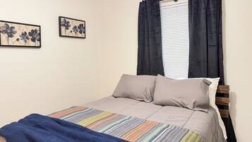 A bedroom with a bed, a window with curtains, and two wall-mounted paintings.