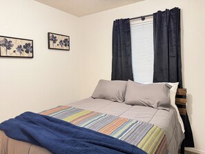 A bedroom with a bed, a window with curtains, and two wall-mounted paintings.