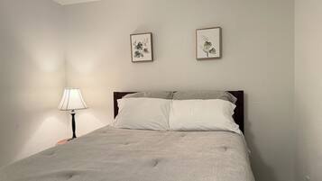 Ein Schlafzimmer mit einem Bett, einem Nachttisch, einer Lampe und zwei gerahmten Bildern an der Wand.