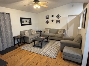 Un salon comprenant un canapé, une table basse, une table d’appoint, un tapis à motifs et un ventilateur de plafond.