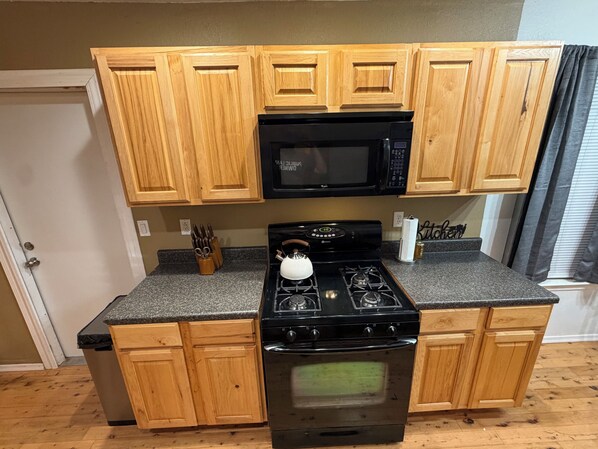 A kitchen with wooden cabinets, a black microwave, a gas stove, and a stainless steel dishwasher.