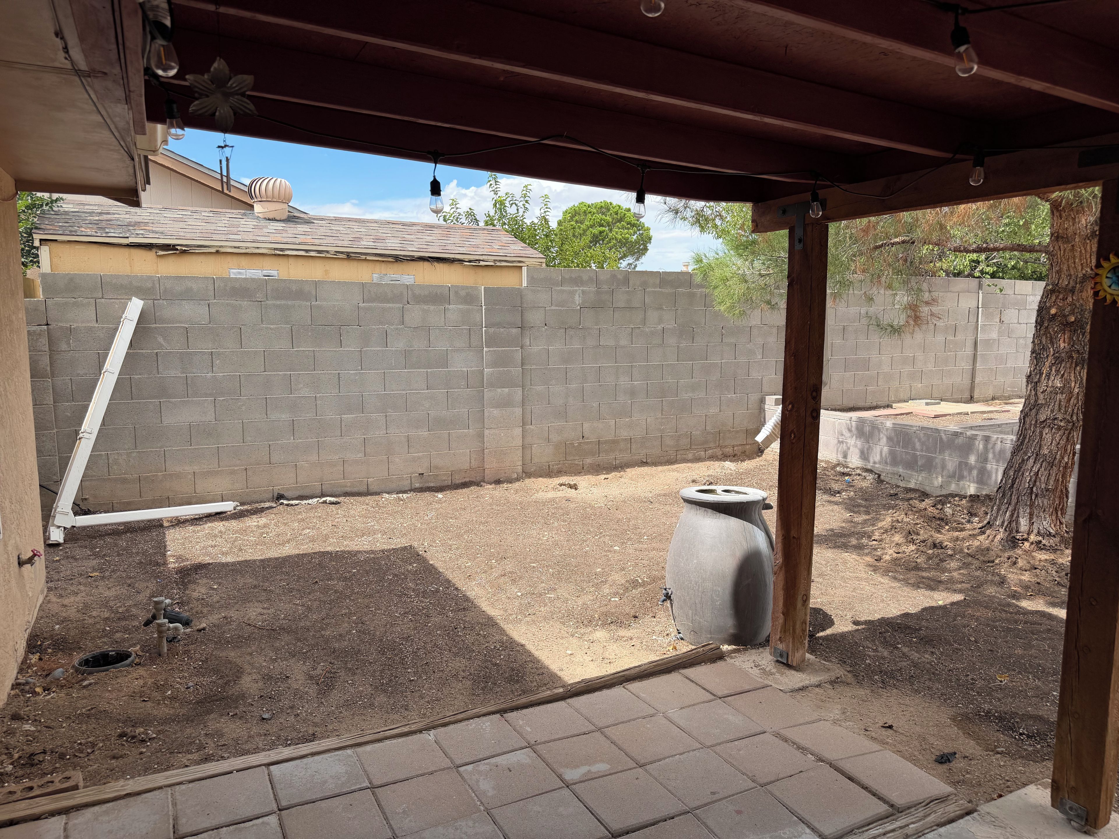 A covered outdoor area with a brick wall, a concrete planter, and a metal pipe.