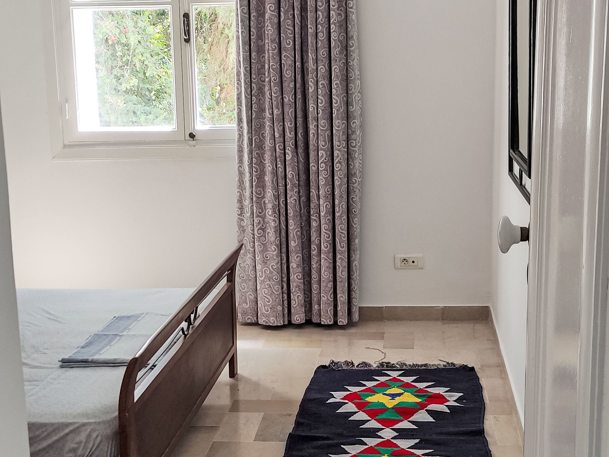 A small room with a bed, a window, a curtain, and a door.