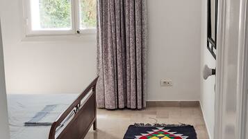 A small room with a bed, a window, a curtain, and a door.