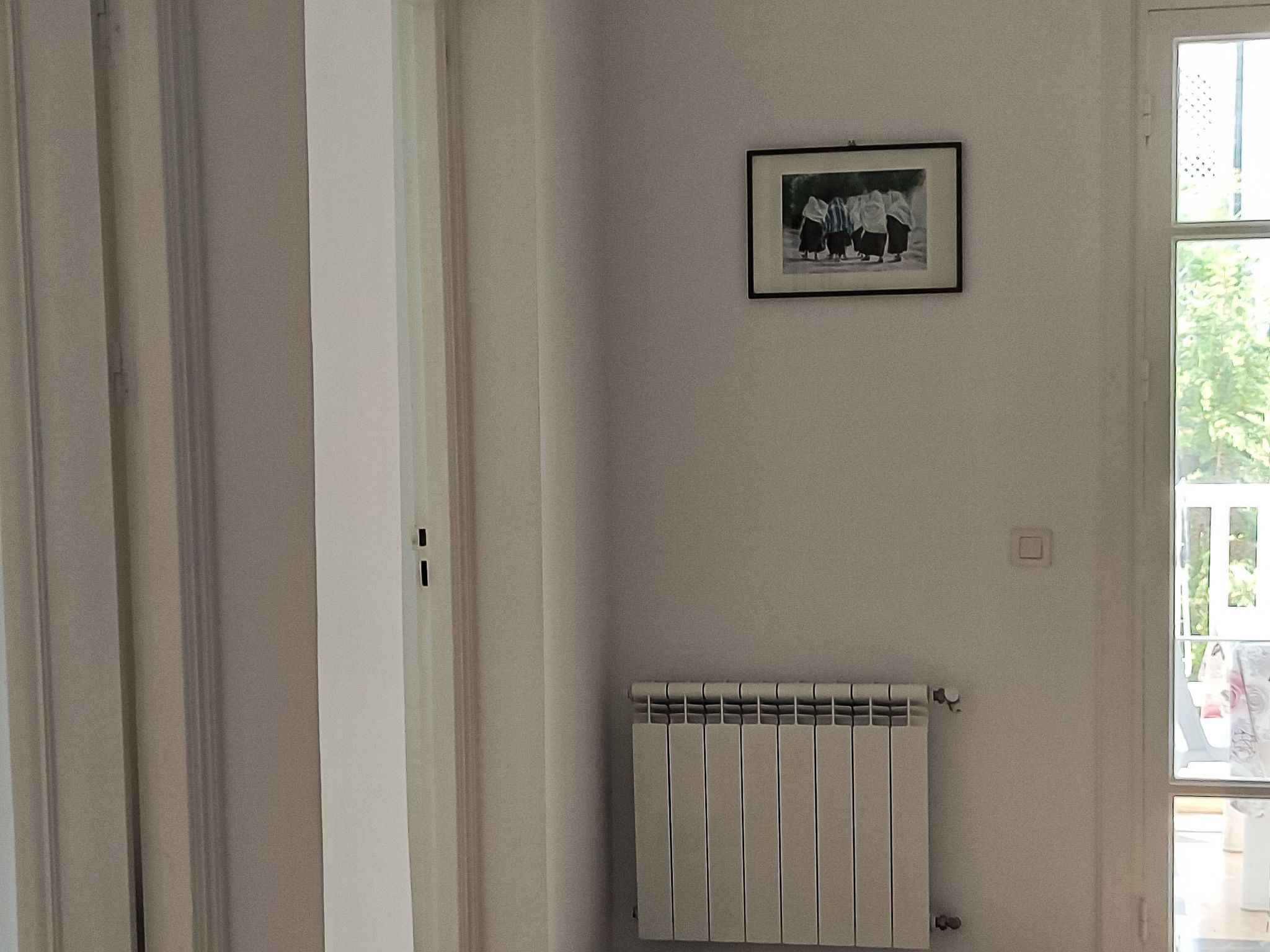 Une pièce avec un radiateur, un tableau encadré au mur et une porte donnant sur un autre espace.