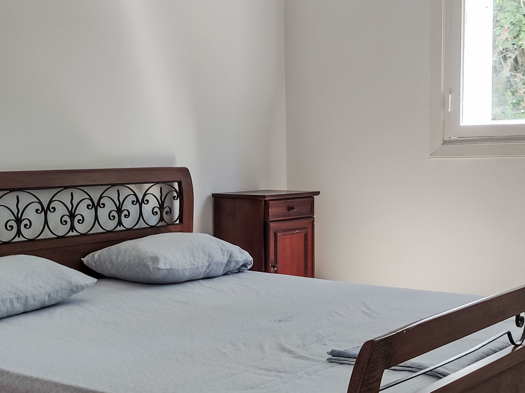 Un dormitorio con cama, almohadas, una mesita de noche y una ventana.