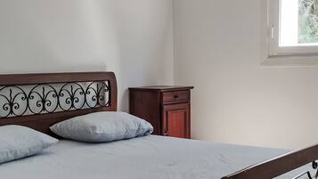 Un dormitorio con cama, almohadas, una mesita de noche y una ventana.