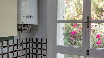 A bathroom with a white tiled wall, a shower area, and a window with a view of pink flowers.