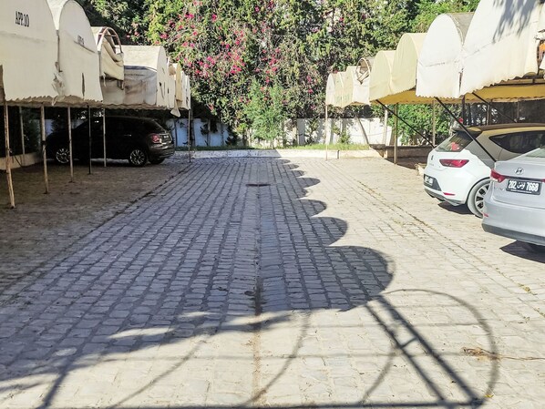 Un cortile pavimentato con auto parcheggiate e un albero con fiori rosa.