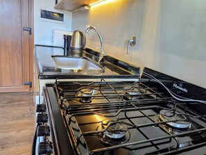 Une cuisine avec un poêle noir, une bouilloire et un évier.