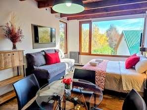 A modern living room with a sofa, a glass table, and a bed with a view of trees. - #3 Monoambiente, buena vista, excelente wifi (San Carlos de Bariloche)