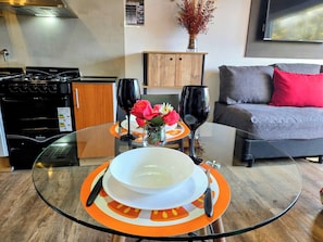 Une cuisine moderne équipée d’une cuisinière à gaz, d’une table à manger avec un plateau en verre et d’un coin salon comprenant un canapé et un vase de fleurs.