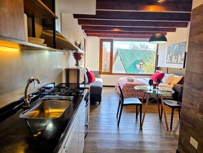 A compact kitchen with a gas stove, a sink, and a dining area with a table and chairs. - #3 Monoambiente, buena vista, excelente wifi (San Carlos de Bariloche)