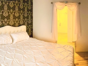 Ein Bett mit weißer Bettdecke und Kissen, einem Kopfteil und einem Vorhang mit einer Lampe.