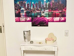 A wall with a cityscape painting, a white console table with a vase, a ring, and a heart-shaped box with roses. - Maritime Perle Bremerhaven by Interhome (Bremerhaven)