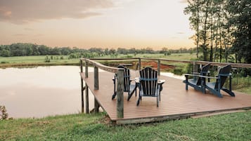 Una terraza de madera con sillas Adirondack con vista a un cuerpo de agua tranquilo y un paisaje boscoso.